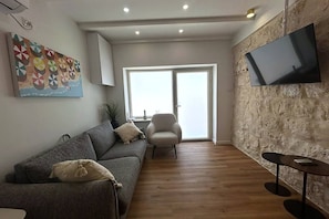 A living room with a sofa, armchair, and a TV mounted on a textured wall. - לופט אורבני ליד המושבה הגרמנת (Haifa)