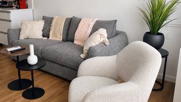 A modern living room with a grey sofa, a white armchair, a small round table with a white vase, and a potted plant.