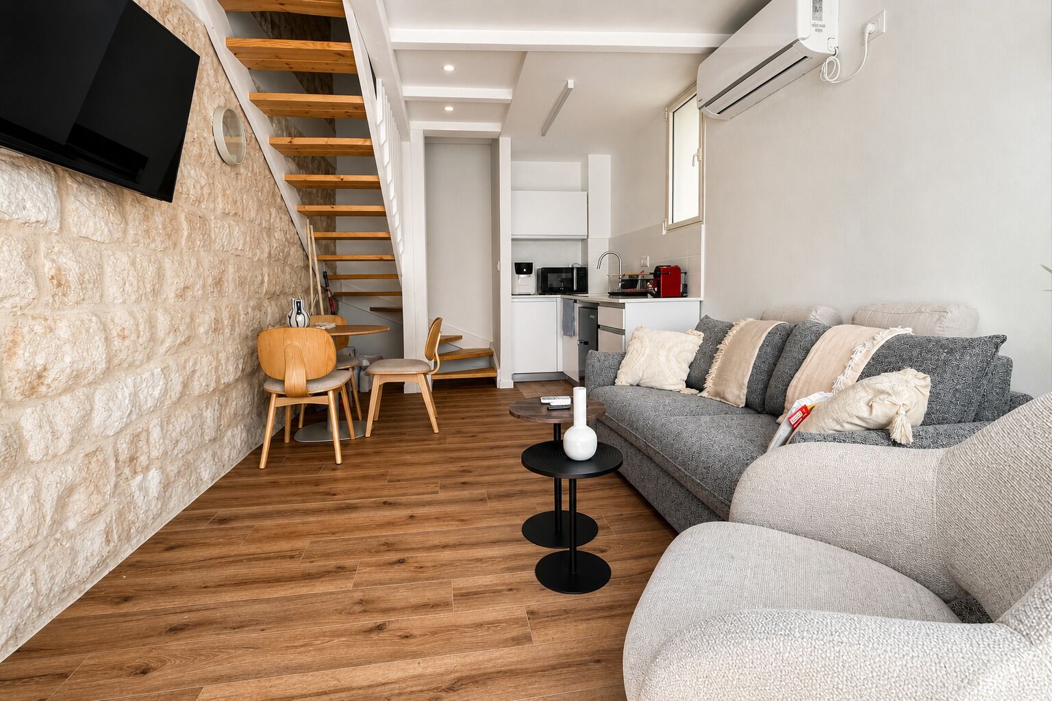 A modern living space with a stone wall, wooden floor, a sofa, a dining table, and a kitchen area.