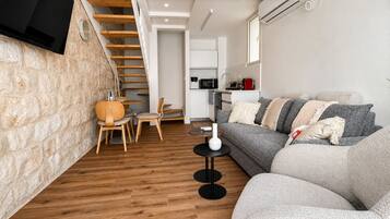 A modern living space with a stone wall, wooden floor, a sofa, a dining table, and a kitchen area.