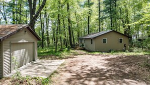 A two-story cabin with a garage, surrounded by a forested area.