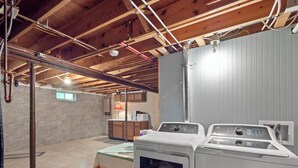 Ein Waschraum mit gestapelten Waschmaschinen und Trocknern, ein Tisch mit Lampe und freiliegende Holzbalken an der Decke.
