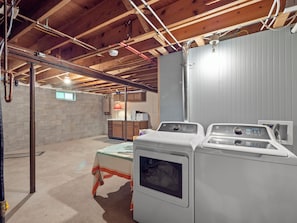 A laundry room with stacked washers and dryers, a table with a lamp, and exposed wooden beams on the ceiling.