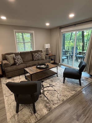 A living room with a sofa, two armchairs, a coffee table, and a view of an outdoor deck. -  NOW BOOKING 2027, start mid May. Upscale Home, 2 Blks to Chain Boat Landing! (Waupaca)