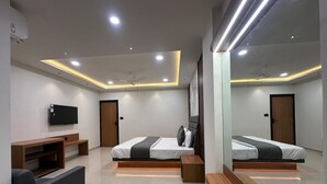 A modern bedroom with a bed, bedside tables, a TV, and a seating area. - Hotel Peacock  (Anand)