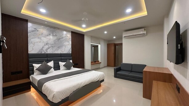 A modern bedroom with a bed, a sofa, an air conditioning unit, and a television. - Hotel Peacock  (Anand)