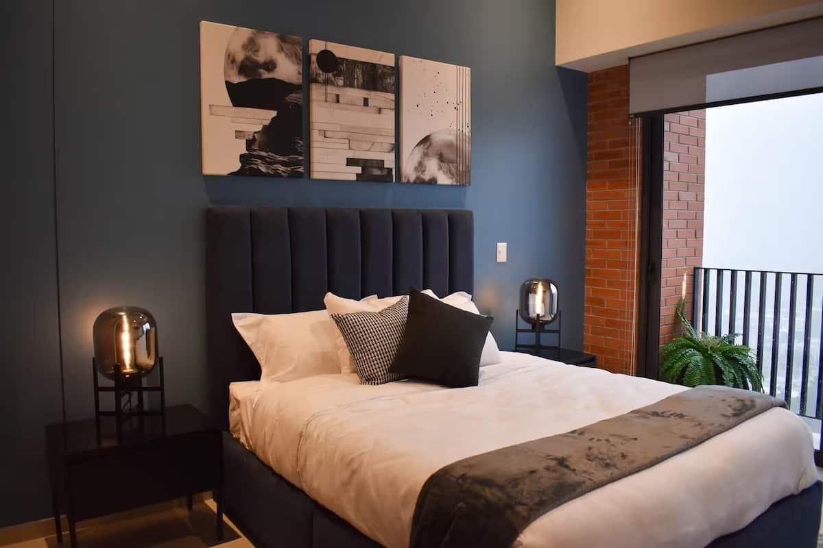 A modern bedroom with a large bed, a headboard, and two wall-mounted lamps.