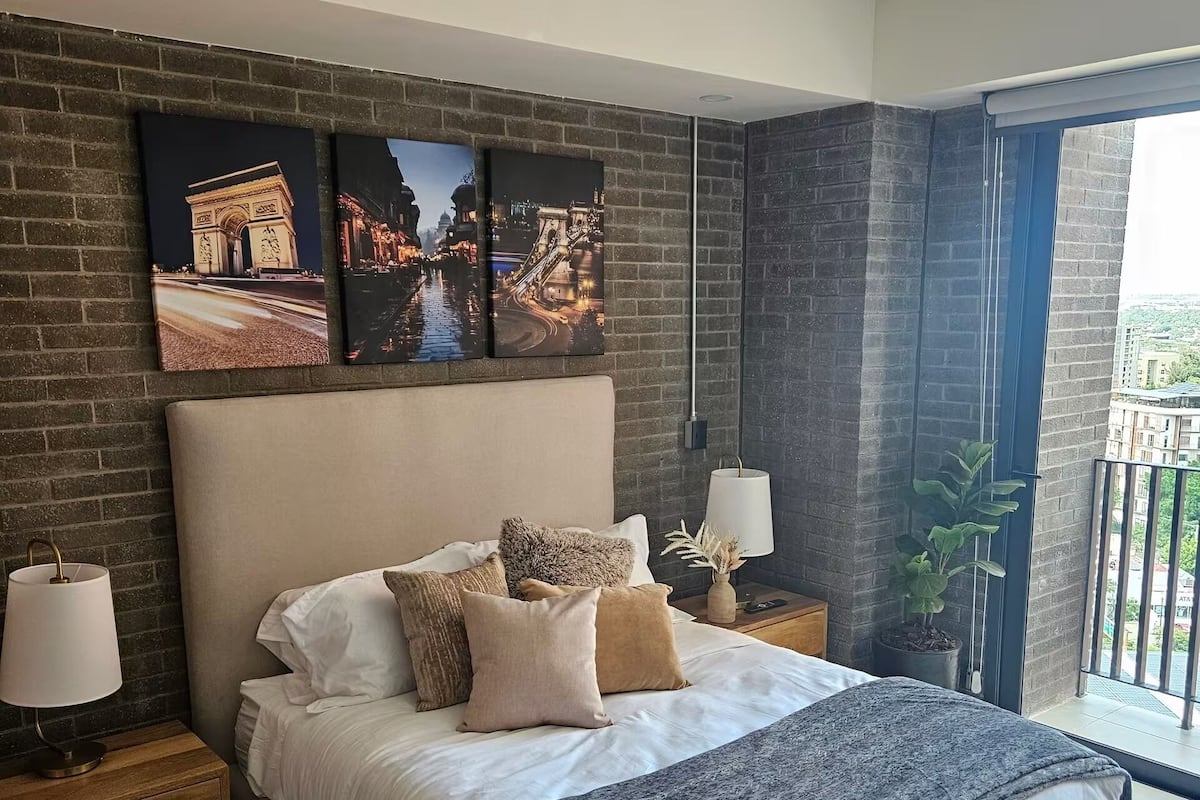 A bedroom with a large bed, a brick wall, and three framed pictures above it.