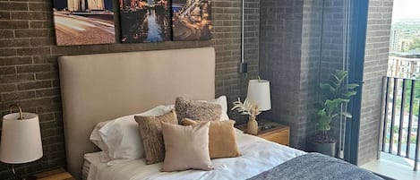 Un dormitorio con una cama grande, una pared de ladrillo y tres cuadros enmarcados encima.