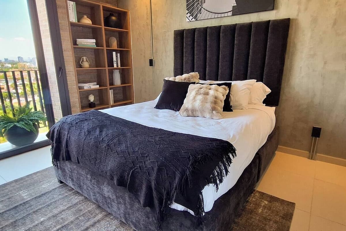A bedroom with a bed, a bookshelf, and a view of the city.