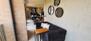 Un espacio moderno de sala con un sofá oscuro, una mesa de centro de madera y una pared de ladrillo.