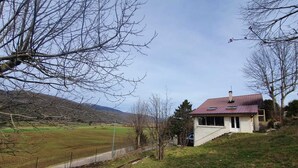 A house with a sloped roof, a chimney, and a view of a hilly landscape. - Old sheepfold surrounded by fields and mountains (La Chapelle-en-Vercors)