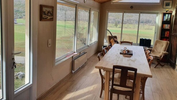 A dining area with a large table, chairs, and a view of the outdoors through large windows. - Old sheepfold surrounded by fields and mountains (La Chapelle-en-Vercors)