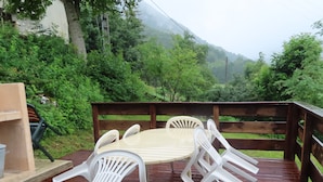A wooden deck with a table and chairs, surrounded by greenery and a mountain in the background. - Old sheepfold surrounded by fields and mountains (La Chapelle-en-Vercors)