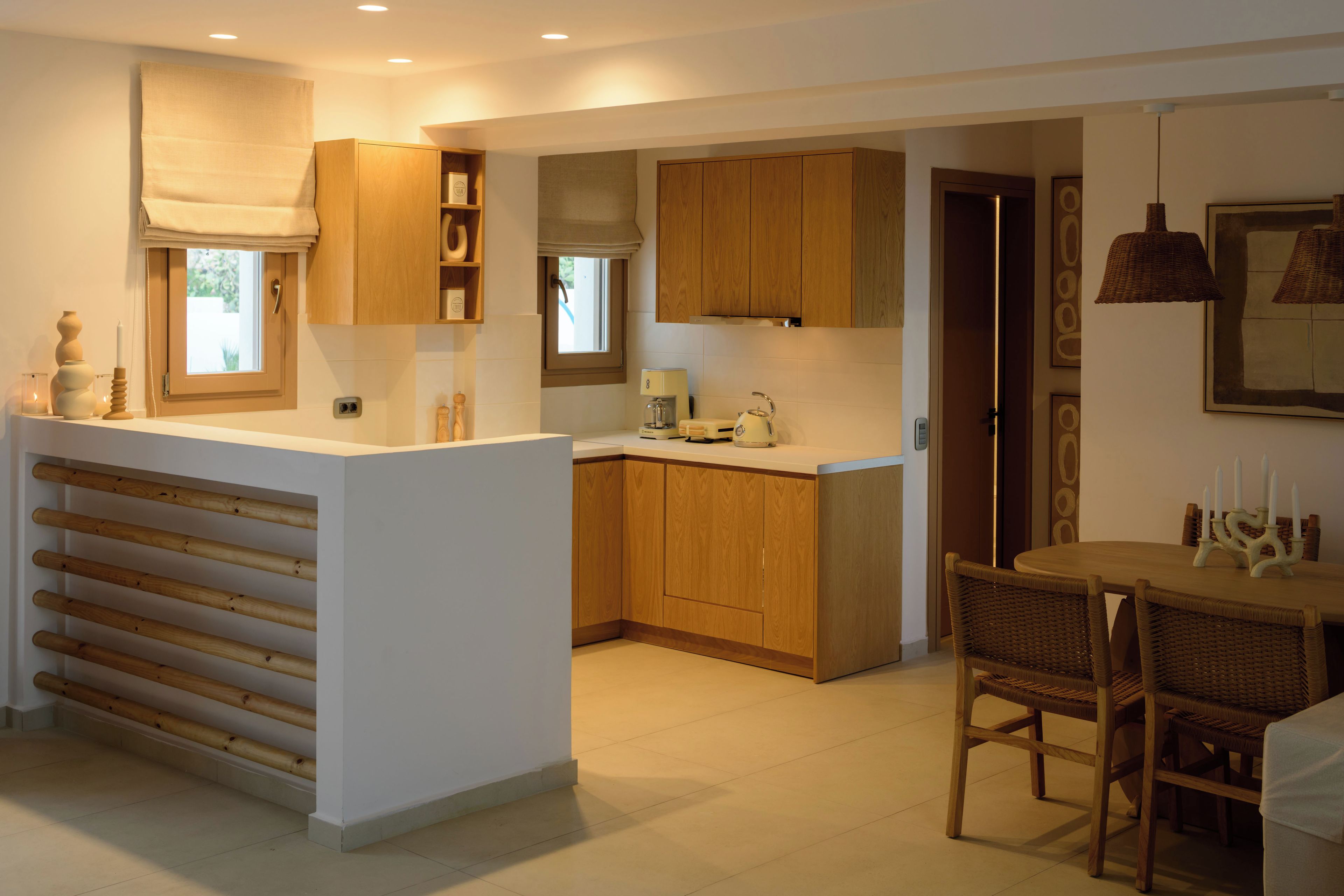 Een moderne keuken met houten kastjes, een centraal eiland en een eethoek met rieten stoelen.