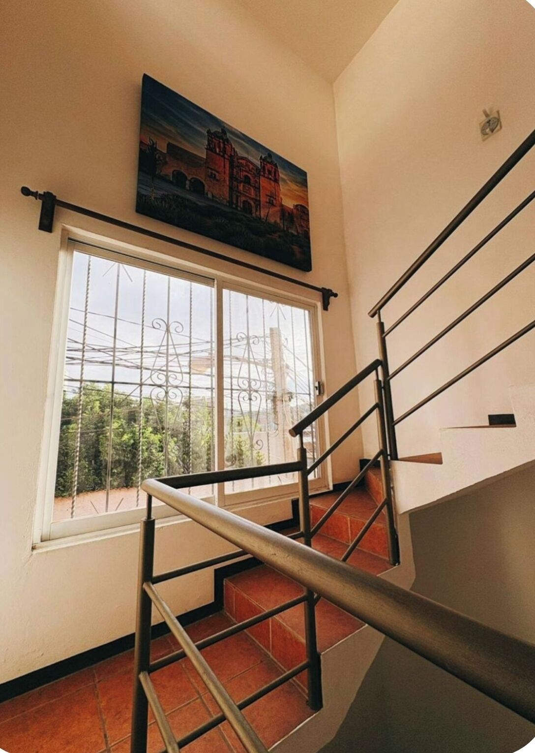A staircase with metal railings leading to a landing, a large window with metal bars, and a painting above the window.