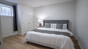 Un dormitorio con cama, mesita de noche, lámpara, ventana con cortinas y puerta.