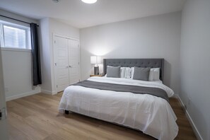 Ein Schlafzimmer mit Bett, Nachttisch, Lampe, einem Fenster mit Vorhängen und einer Tür.