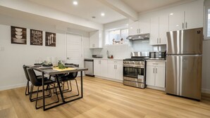 Una cocina moderna con armarios blancos, electrodomésticos de acero inoxidable y una zona de comedor con sillas negras.