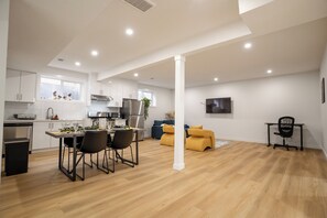 Eine moderne Küche mit weißen Schränken, ein Essbereich mit Tisch und Stühlen sowie ein Wohnbereich mit einer Couch und einem an der Wand befestigten Fernseher.