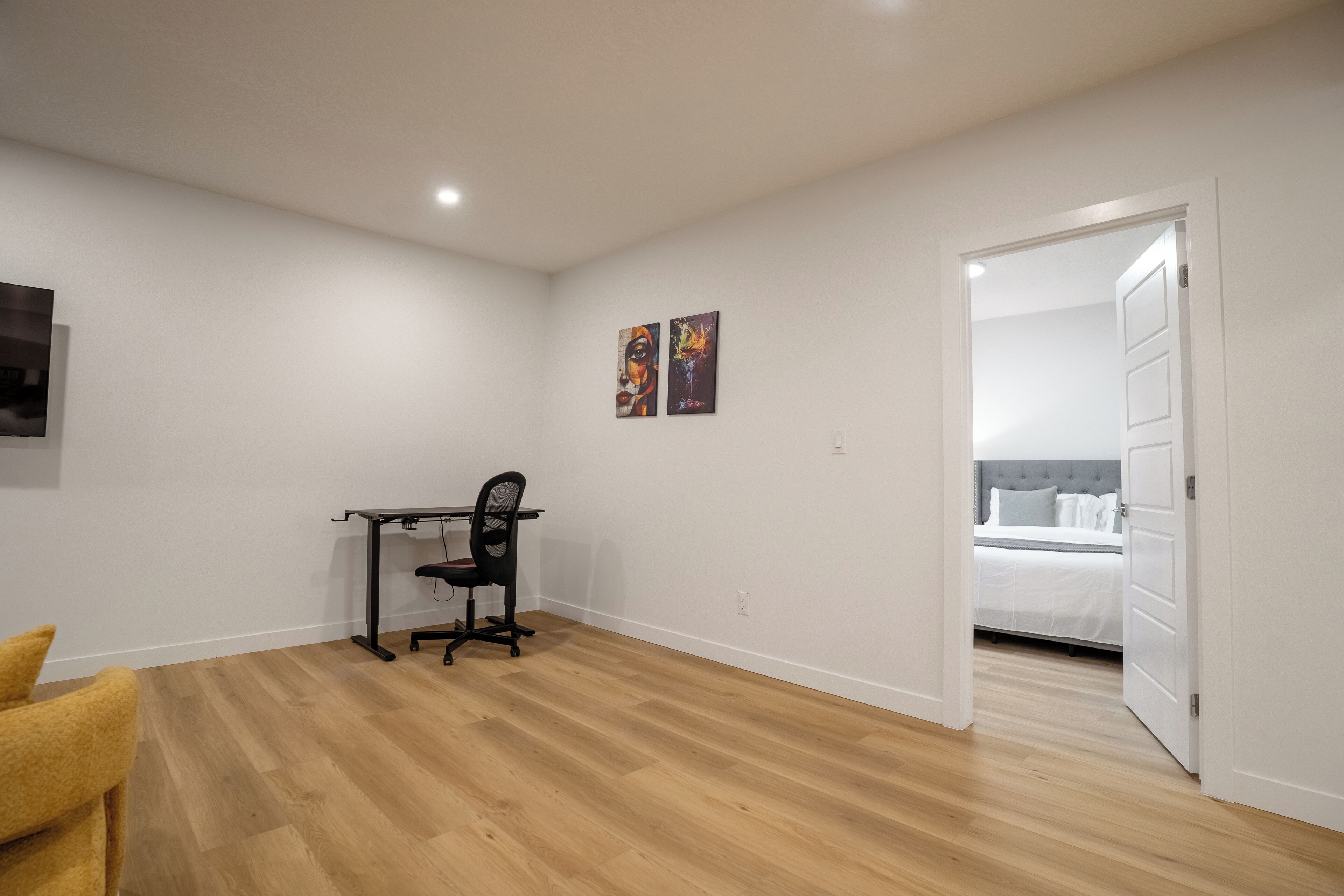Een slaapkamer met een bed, een bureau met stoel, en twee schilderijen aan de muur.