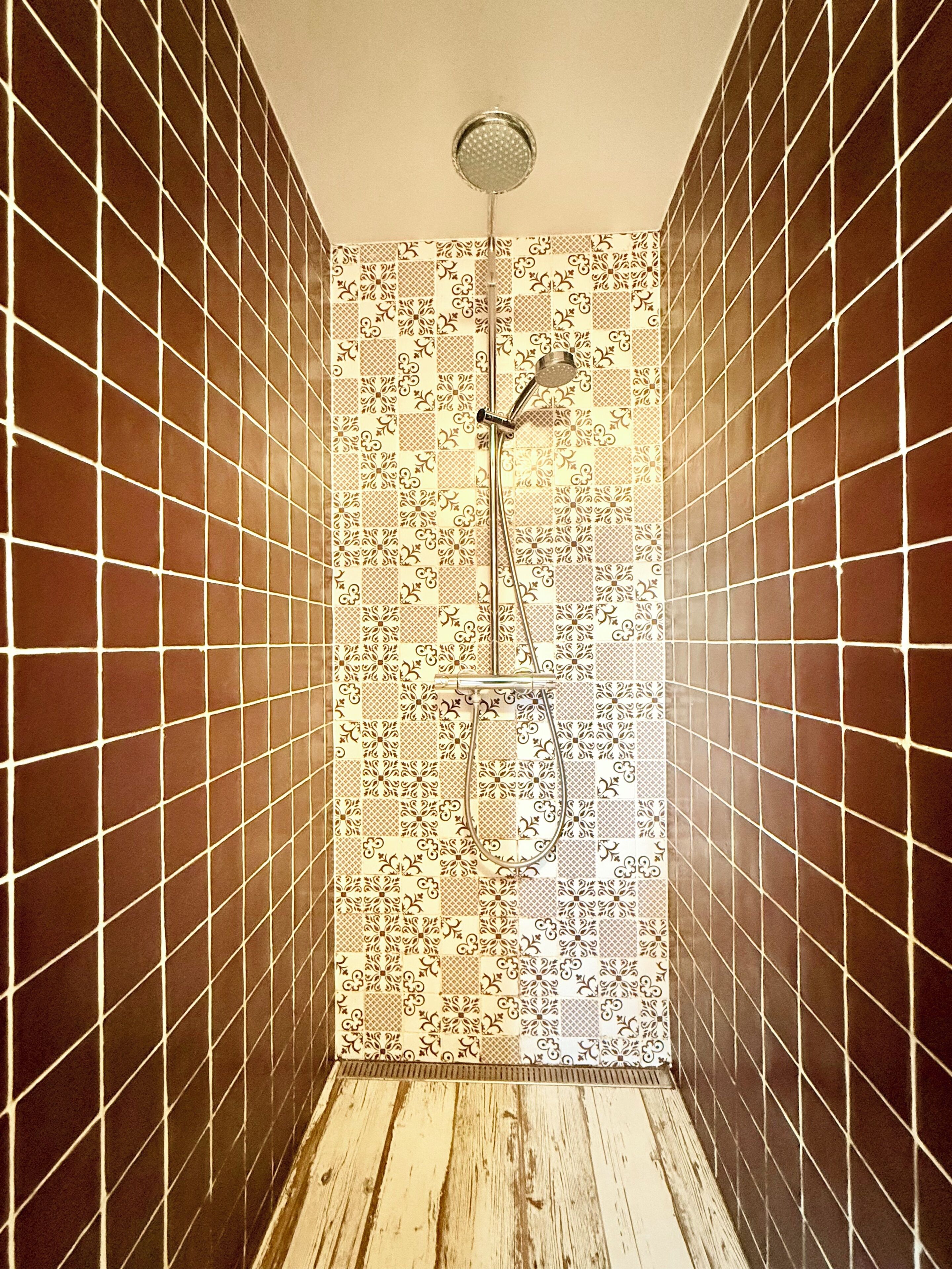 Ducha con pared de azulejos estampados y suelo de madera.
