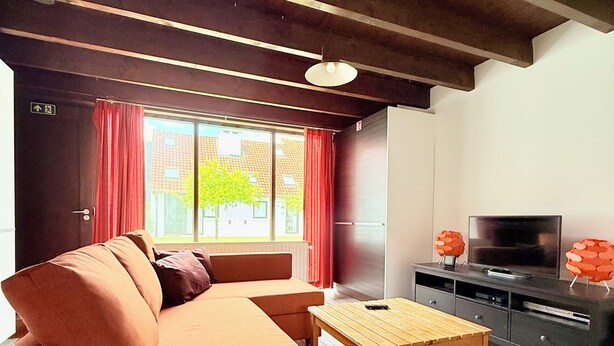 Ett modernt vardagsrum med en soffa, ett soffbord, en tv och ett fönster med gardiner.