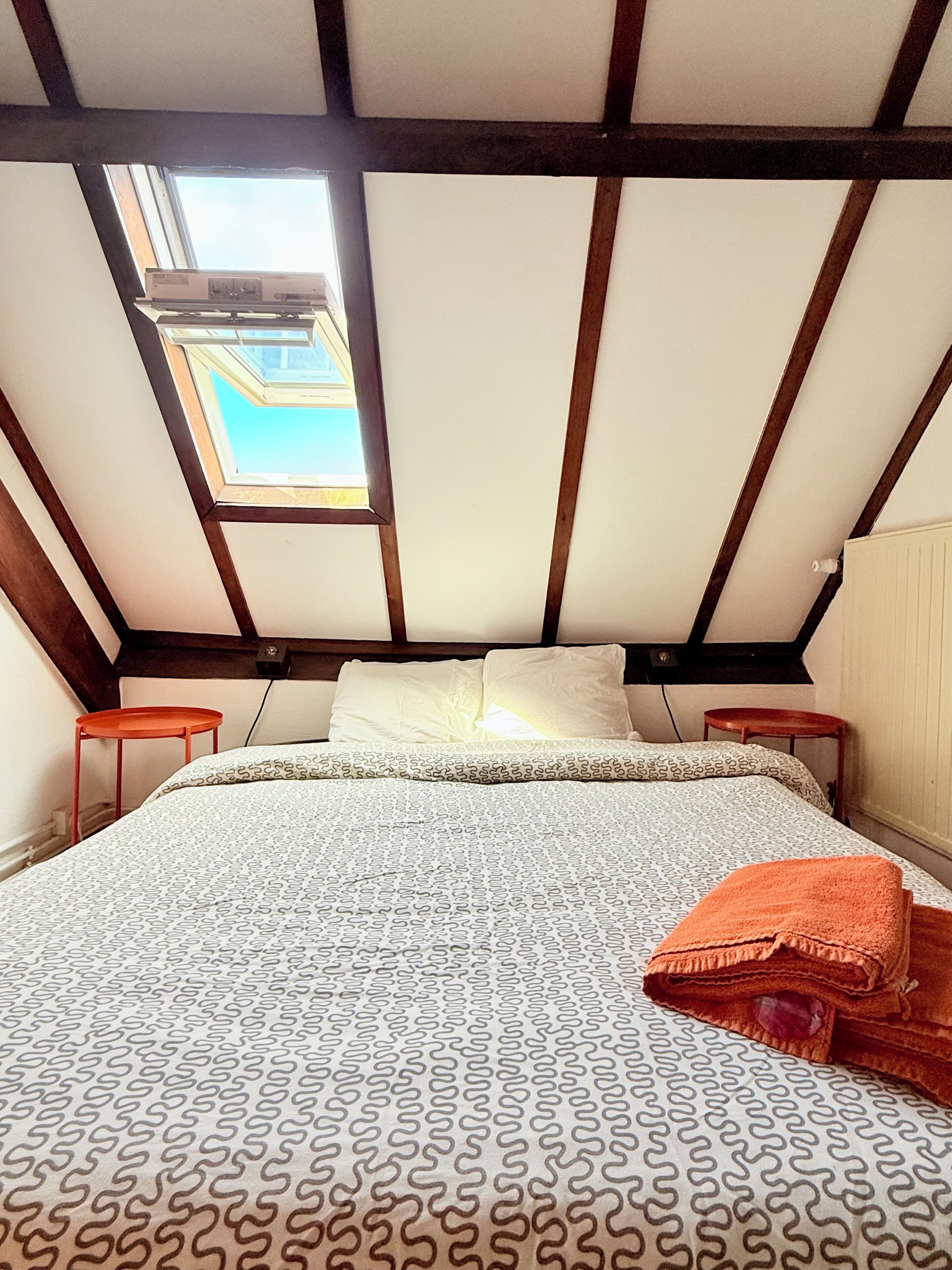 Una habitación con techo inclinado, tragaluces, una cama con ropa de cama estampada y dos mesitas de noche.
