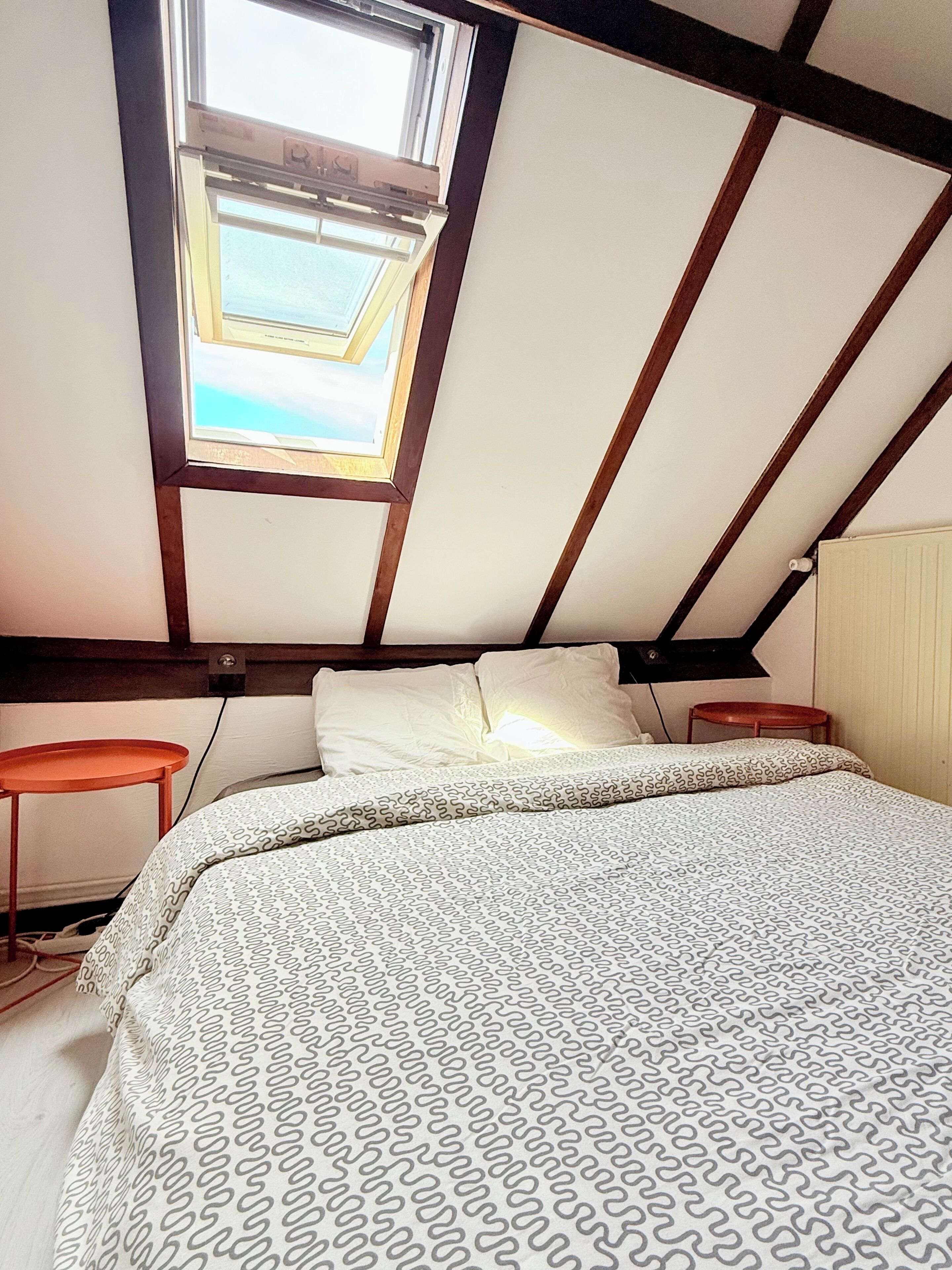 Een slaapkamer met dakraam, een bed met beddengoed met patroon, een nachtkastje en een bijzettafeltje.