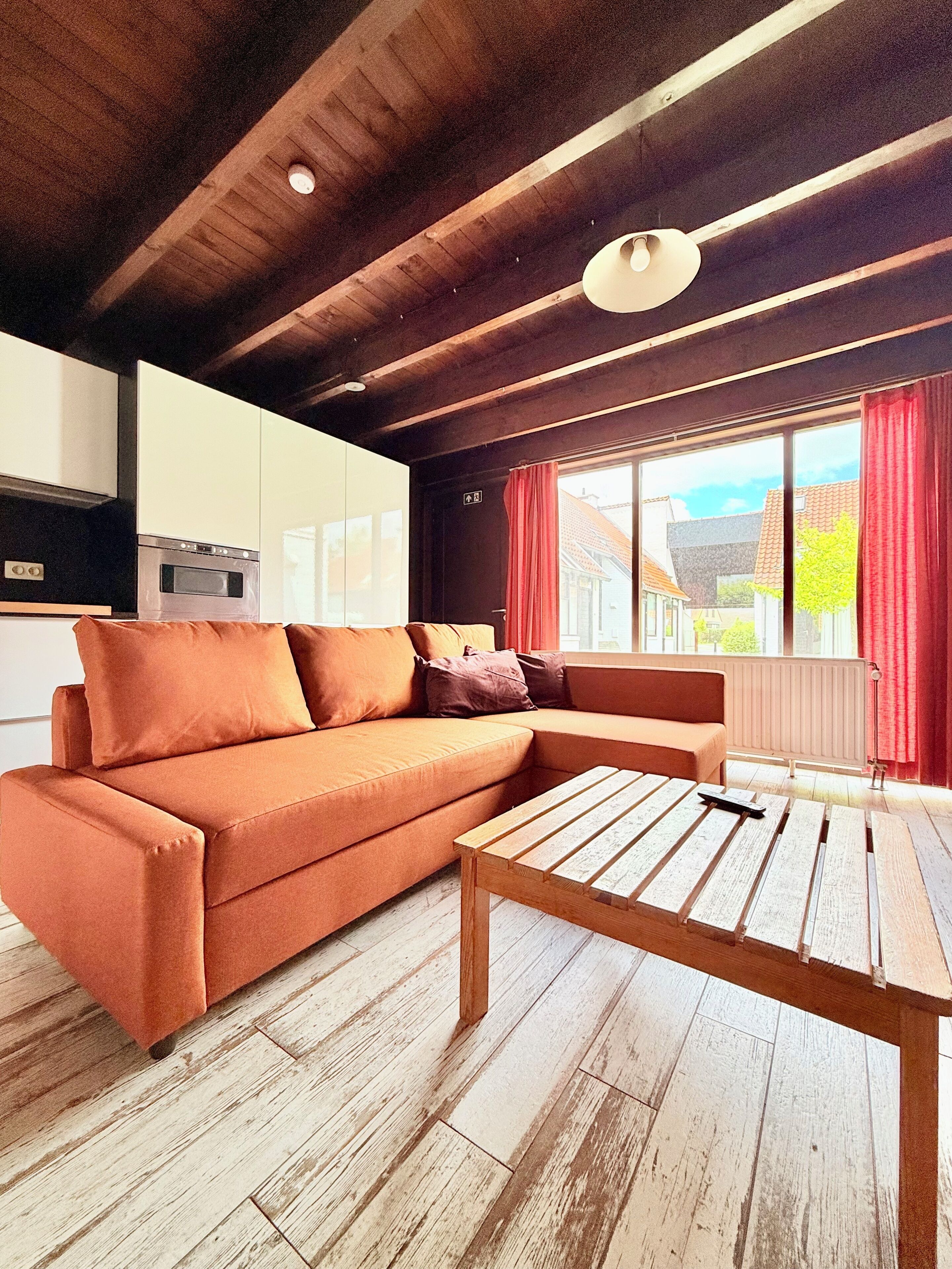 Una sala de estar moderna con un sofá, una mesa de centro de madera y vistas al exterior a través de amplios ventanales.