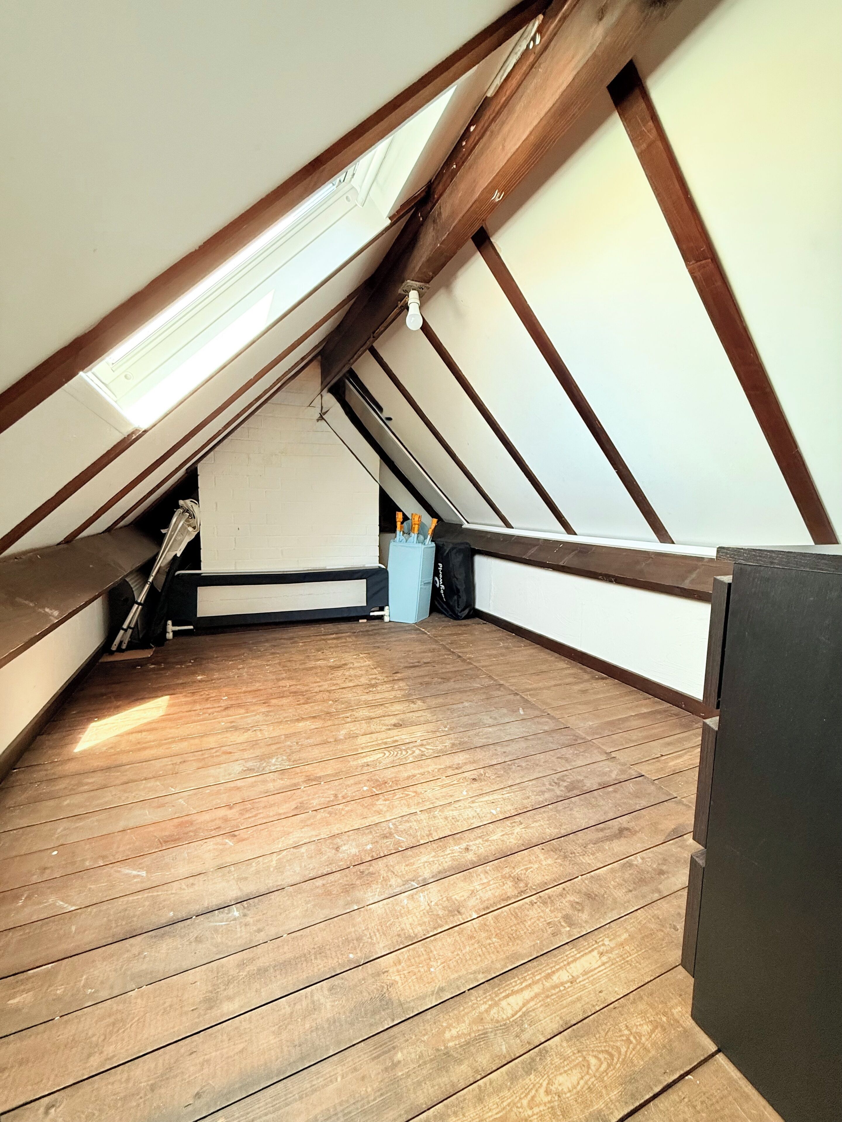 An attic room with wooden beams, a slanted ceiling, and a skylight.
