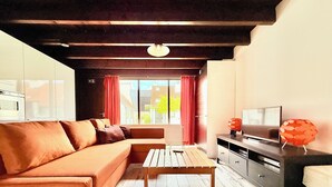 Ett modernt vardagsrum med en soffa, ett soffbord i trä, en tv på ett tv-bord och ett fönster med gardiner.