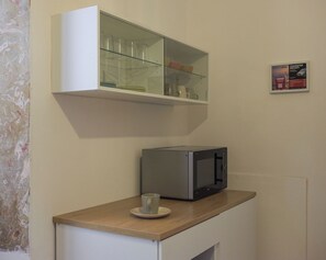 A kitchenette with a microwave, a glass cabinet above it, and a small cup on the counter. - Dimora Giardino di Giulietta (Verona)