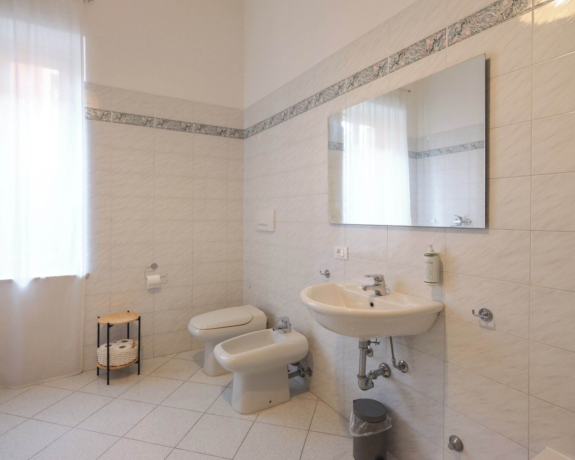 Et badeværelse med toilet, bidet, håndvask og spejl.