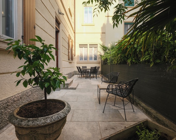 A patio with a table and chairs, a potted plant, and a wall with climbing plants.