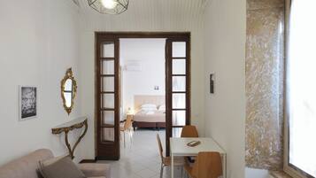 A hotel room with a bed, a dining table with chairs, a sofa, a mirror, and a hanging light fixture.
