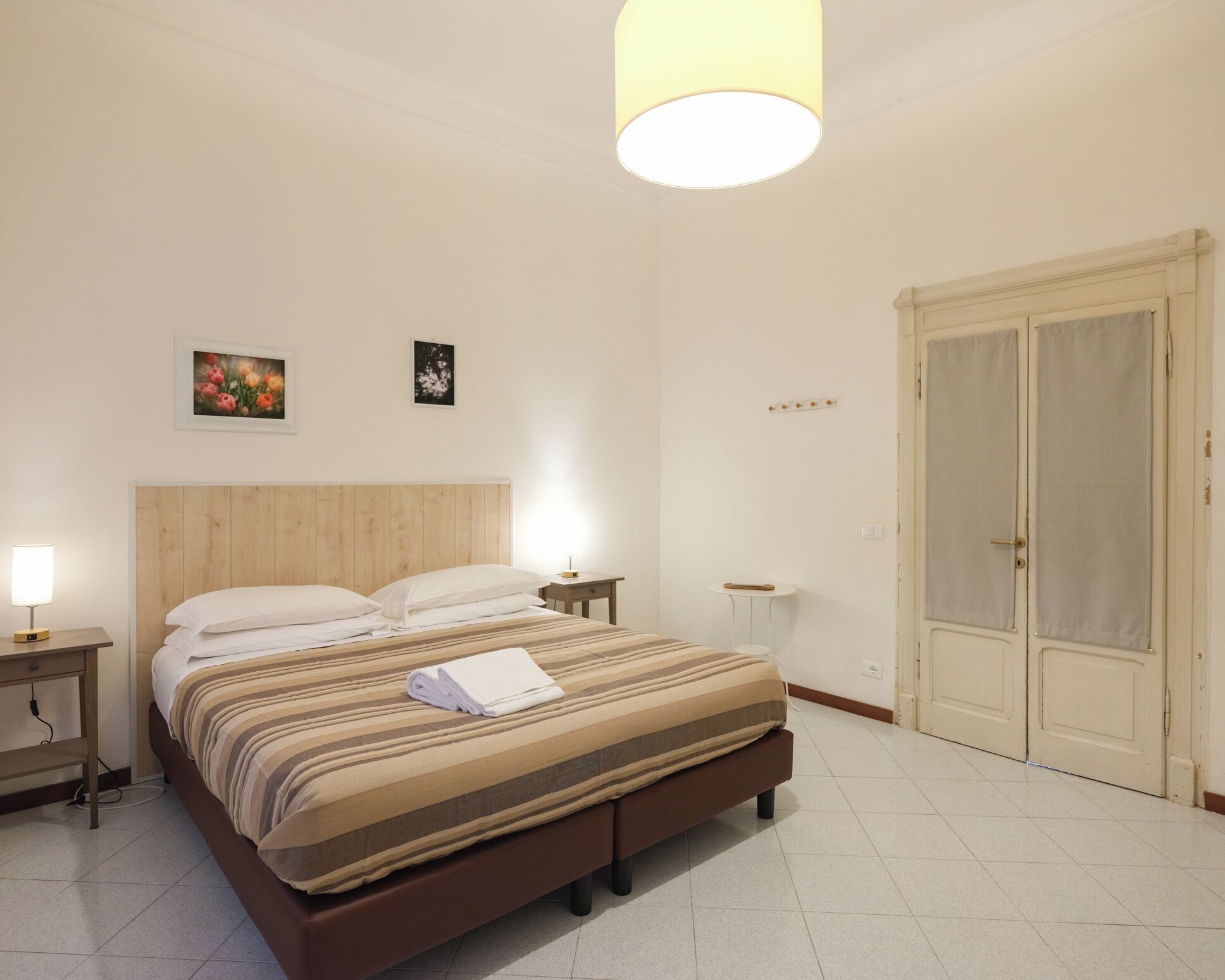 A bedroom with a bed, bedside tables, a nightstand, a lamp, a wardrobe, and a ceiling light.