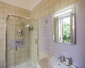 A bathroom with a glass shower enclosure, a sink with a mirror, and a wall-mounted informational sign. - Dimora Giardino di Giulietta (Verona)