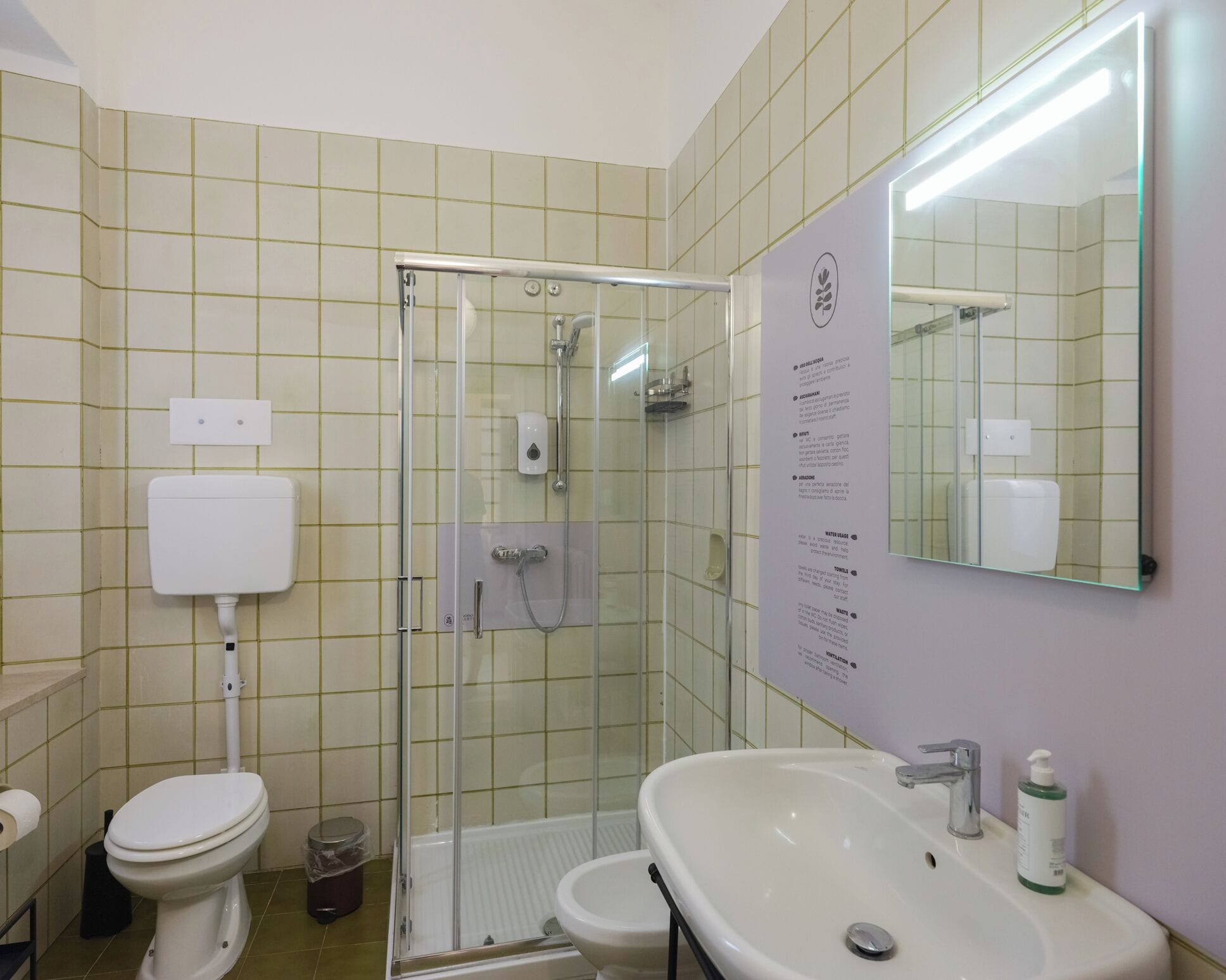 A bathroom with a toilet, sink, shower, and a mirror.