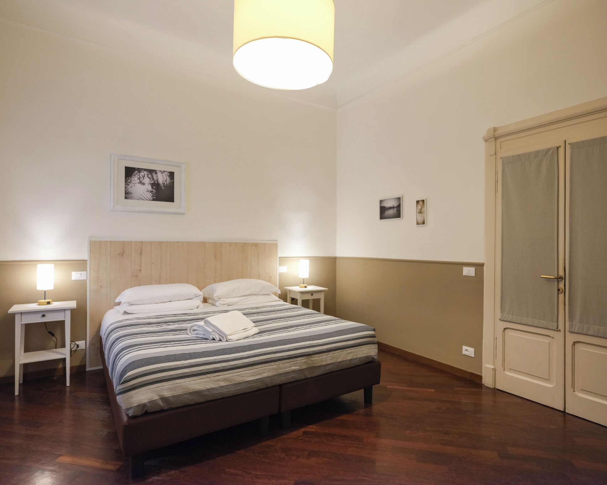 A bedroom with a bed, bedside lamps, a wooden headboard, a door, and a wall-mounted picture.
