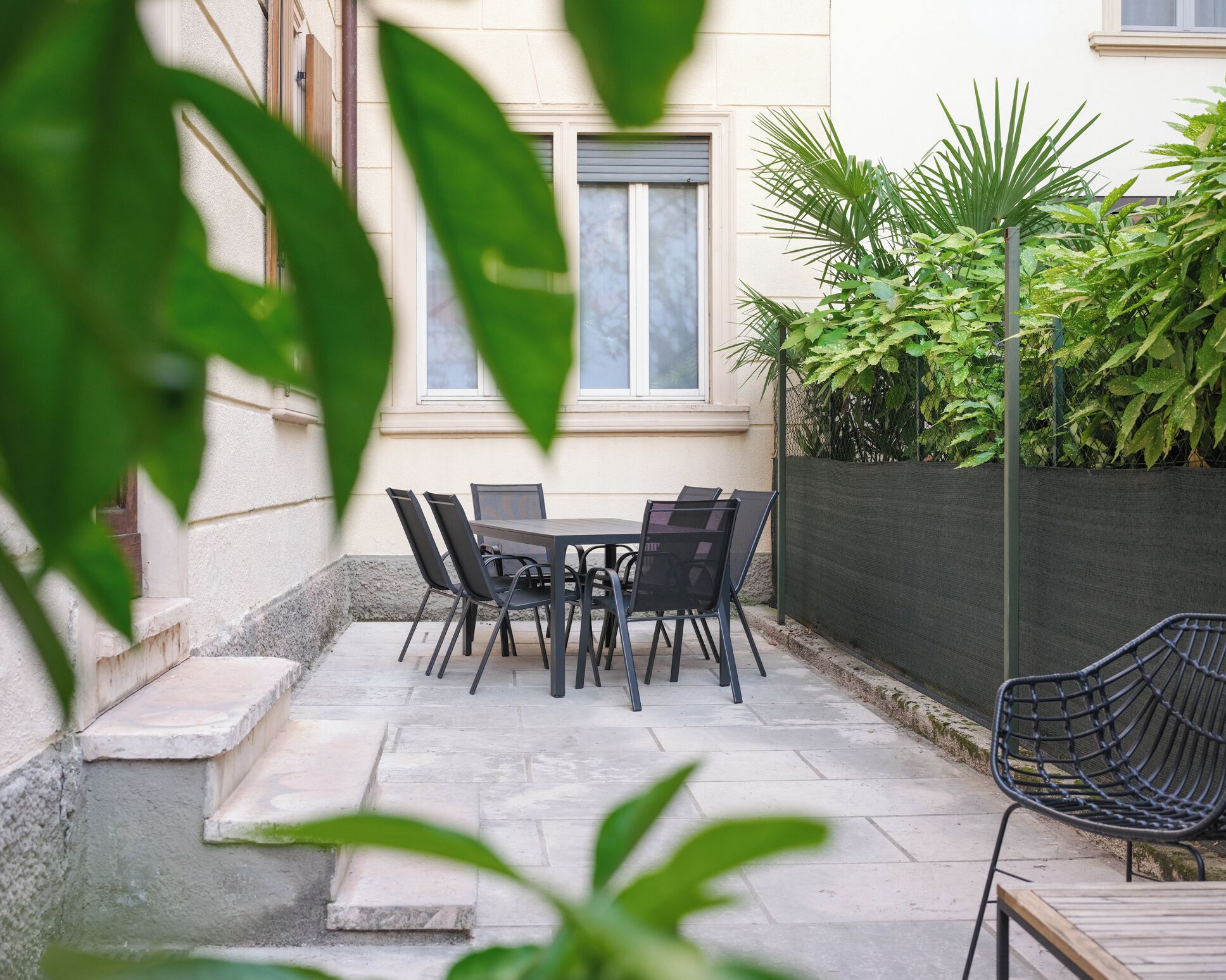 En terrasse med et bord og stole, en lille trappe og mange forskellige planter.