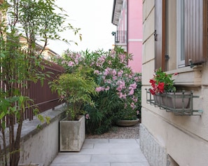 A narrow pathway flanked by a concrete planter and a building with a pink facade.