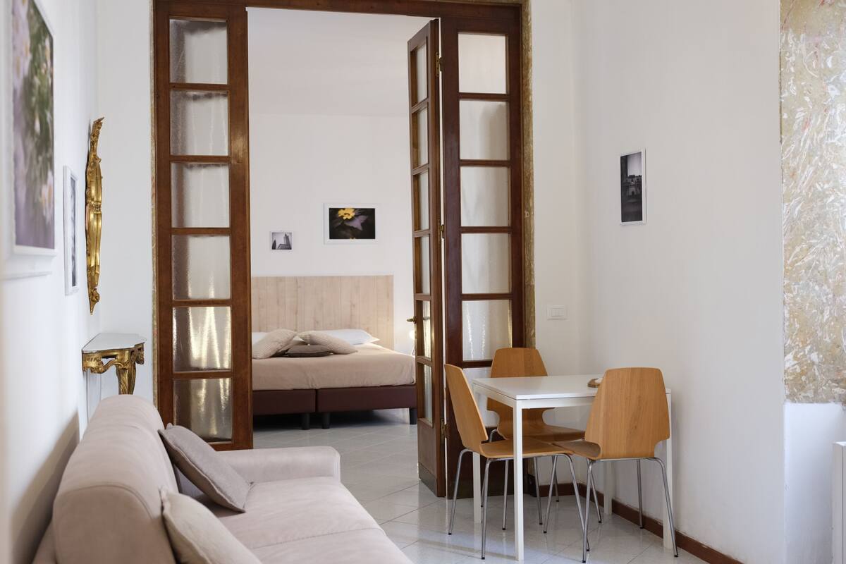 Una habitación con una cama, un sofá, una mesa de comedor con sillas y una puerta que da a otra habitación.