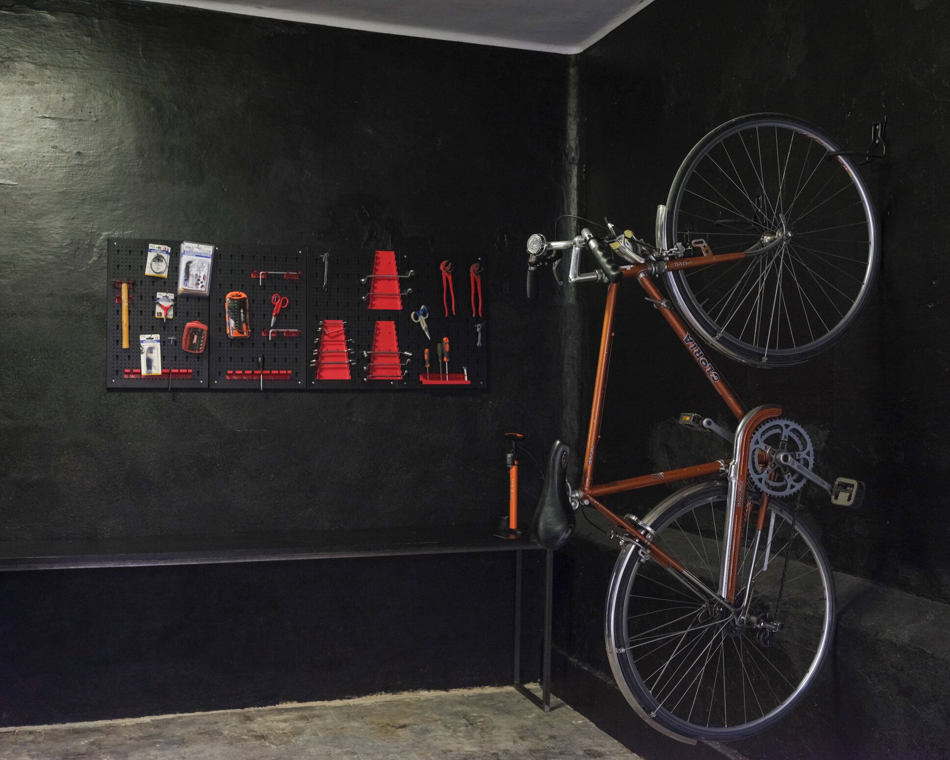 A bicycle mounted on a wall with tools and equipment displayed below.
