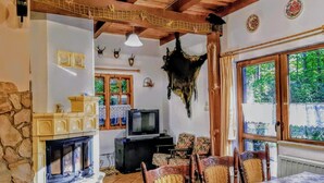 Un interior rústico con chimenea de piedra, vigas de madera en el techo, un televisor y un comedor con sillas.
