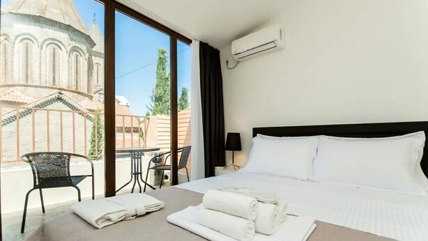 Habitación de hotel con cama, una mesa, sillas, equipo de aire acondicionado y vista a un edificio.