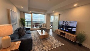 A modern living room with a sofa, coffee table, TV, and large windows offering a city view. - Halifax waterfront 2 BR/2 Bath with 6 appliances (Halifax)