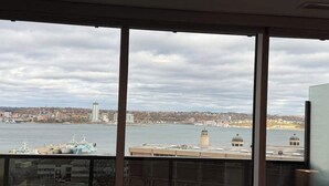 A view from a high-rise room with large windows overlooking a body of water, a city skyline, and a distant tower. - Halifax waterfront 2 BR/2 Bath with 6 appliances (Halifax)