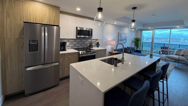 A modern kitchen with a stainless steel refrigerator, a built-in oven, and a large island with bar stools. - Halifax waterfront 2 BR/2 Bath with 6 appliances (Halifax)