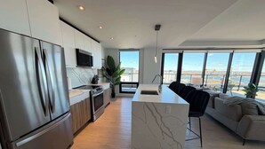 A modern kitchen with stainless steel appliances, a marble island, and a large window overlooking a cityscape. - Waterview 2 BR / 2 Bath penthouse in Northend HFX. (Halifax)